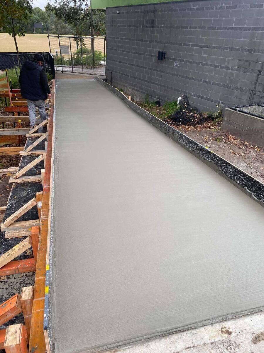 Concreter checking a freshly poured footpath still boxed in formwork
