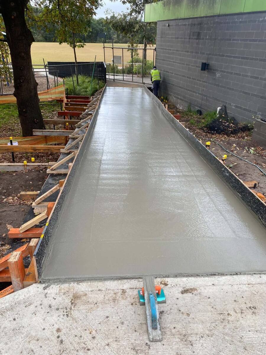 Fresh concrete footpath with a smooth trowelled finish beside a brick wall